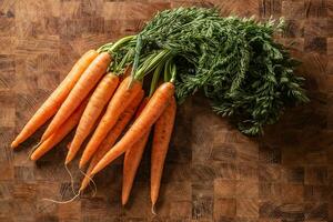 Fresh carrots with tops placed on a vintage wooden surface photo