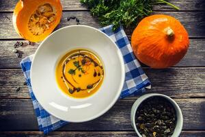 Pumpkin cream soup with seeds and parsley on kitchen table - Top of view photo