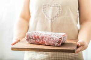 Female cook holding wooden board of raw and frozen beef  meat photo