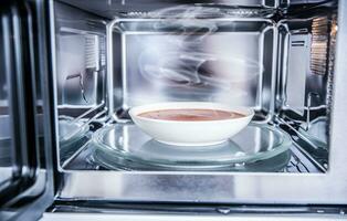 Inside view of new clean staniless microwave oven with a tomato soup in white plate photo