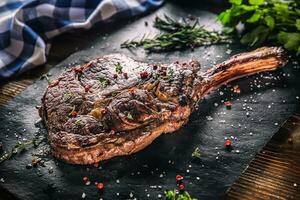 Freshly grilled tomahawk steak on slate plate with salt pepper rosemary and parsley herbs photo