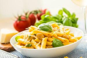 Pasta penne with chicken pieces mushrooms basil parmesan cheese and white wine.  Italian food in white plate on kitchen table photo