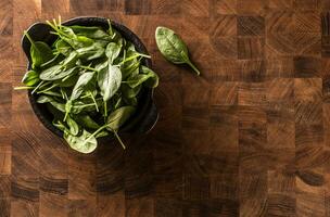 Fresh baby spinach leaves in bowl on butcher board photo