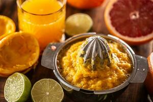 exprimido naranja pulpa en un exprimidor con recién cortar cítricos y un vaso de jugo foto