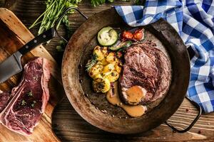 Juicy beef Rib Eye steak roasted potatoes with sauce grilled vegetable salt pepper and herbs in vintage pan photo