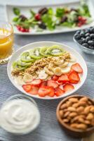 Healthy breakfast served with plate of yogurt muesli kiwi strawberries and banana photo