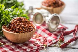 Dried and crushed chili peppers in wooden bowles with parsley herbs photo