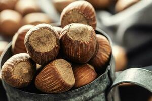 Close up of a vintage metallic mug full of hazelnuts with more nuts on a textile table cloth around it photo