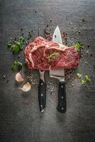 Raw beef steak with fork and knife salt pepper and herbs on dark concrete background photo