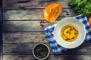 Pumpkin cream soup with seeds and parsley on kitchen table - Top of view photo