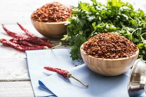 Dried and crushed chili peppers in wooden bowles with parsley herbs photo