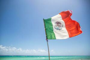 Mexican flag partially ripped by the wind blowing from the turquiose Carribean Sea photo