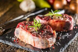 Two pieces raw beef shank on slate board and wooden table. photo