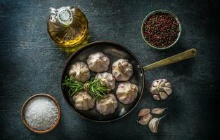 Garlic cloves and bulb in pan with fresh rosemary olive oil salt and spice on concrete table photo