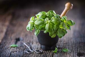 Fres basil leaves in mortar on wooden table photo