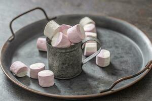 Metallic vintage tray, surface and cup with pink and white marshmallows inside the cup and scattered around the tray photo