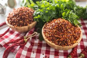 Dried and crushed chili peppers in wooden bowles with parsley herbs photo