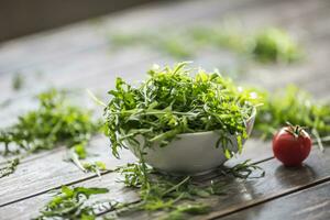 Fresh arugula salad in white dish on wooden table photo