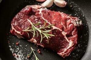 Fresh raw beef Ribe Eye steak in teflon pan with rosemary, garlic, salt and pepper photo