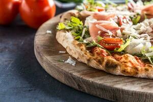 Italian pizza with prosciutto arugula tomatoes and parmesan on wooden round board photo