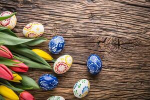 Easter. Hand made easter eggs and spring tulips on old wooden table. photo