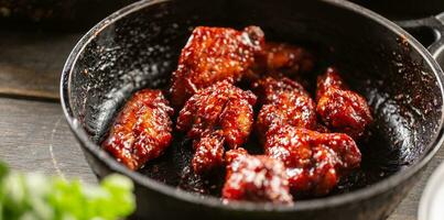 Spicy glazed marinated chicken wings in a dark pan photo