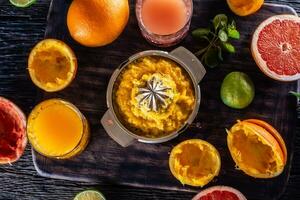 Top view of juicer full of orange pulp with fresh citruses, juices and fruit skins around photo