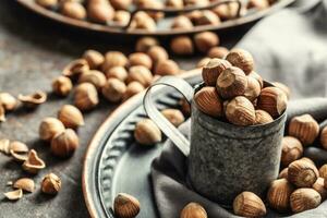 Hazelnuts and their cracked shells on a vintage dark metallic background, in a metallic cup and on a tray with a cloth photo