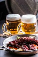 Grilled hot sausages served in a hot pan next to two draft beers photo