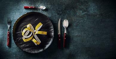 Dark plate with measure tape, next to it cutlery. Top of view on concept healthy eating photo