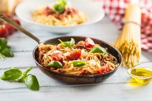 Italian pasta spaghetti bolognese in old pan with tomatoes parmesan cheese and basil photo