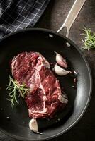 Fresh raw beef Ribe Eye steak in teflon pan with rosemary, garlic, salt and pepper photo