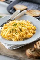 Tasty yellow freshly-made scrambled eggs with chives in a plate, served with toasted bread slices photo