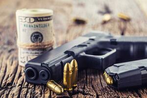 Gun and money. 9 mm pistol gun bullets strewn and roll dollar banknotes on rustic oak table photo