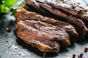 recién A la parrilla carne de vaca filete en pizarra plato con sal pimienta Romero y perejil hierbas. rebanado piezas de jugoso carne de vaca filete foto