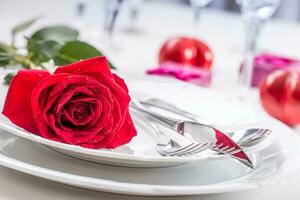 Table setting for valentines or wedding day with red roses. Romantic table setting for two with roses plates cups and cutlery photo