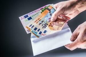 Male hand inserted into the envelope euro banknotes - bribe and corruption concept. photo