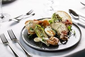 A twist of an elegant ceasar salad with shrimps served on a dark plate in a restaurant photo