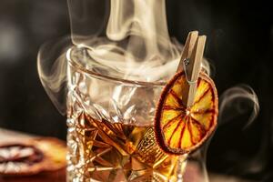 Smoked old fashioned rum cocktail with cubes of ice around on a dark background. photo