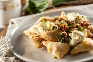 Fried pierogi served on a plate with bryndza cheese, bacon, and chives photo