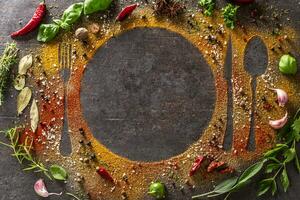 Spices and herbs scattered on the table forming the silhouette of cutlery and a plate. photo