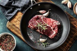 Fresh raw beef Ribe Eye steak in teflon pan with rosemary, garlic, salt and pepper photo