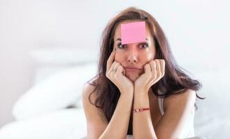 Woman who forgot something has pink postit on her forehead holding her head with both heads, thinking hard photo