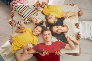 Family holds the same picture of themselves while lying on the floor, smiling photo