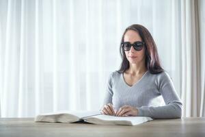 Woman with congenital blindness reads book in braille on a table in front of her photo