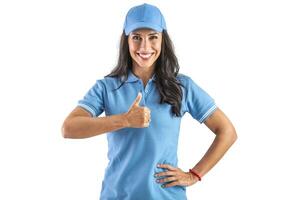 Young attractive woman in blue uniform widely smiling and holding her thumb up in front of her chest. probably working in parcel shop. Isolated background photo