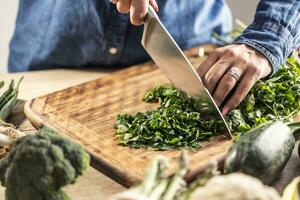 Detail of female hands holding a knife and chopping fresh parsley greens photo