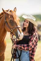 Beautiful girl in a cowgirl wear smiles at her brown horse photo