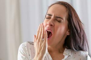 Tired and sleepy woman yawns with mouth wide open and a hand in front of her mouth photo