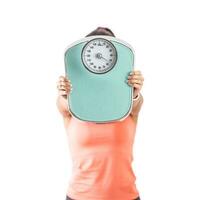 Woman holds a weighing scale against the camera covering her face with it photo